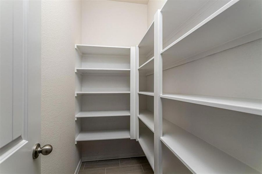 Keep your kitchen essentials neatly organized in this spacious pantry, featuring built-in shelving that provides ample storage for all your dry goods and supplies. Photos are from another Rylan floor plan.