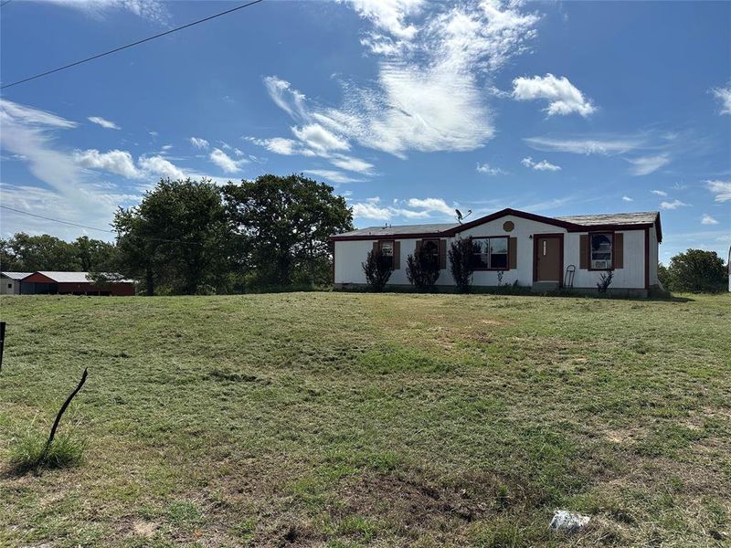 Spacious lot with a white single-story residence featuring a brown trim roof, multiple windows with brown shutters, and a front entry door Spacious lot with a white single-story residence featuring a brown trim roof, multiple windows with brown shutters, and a front entry door