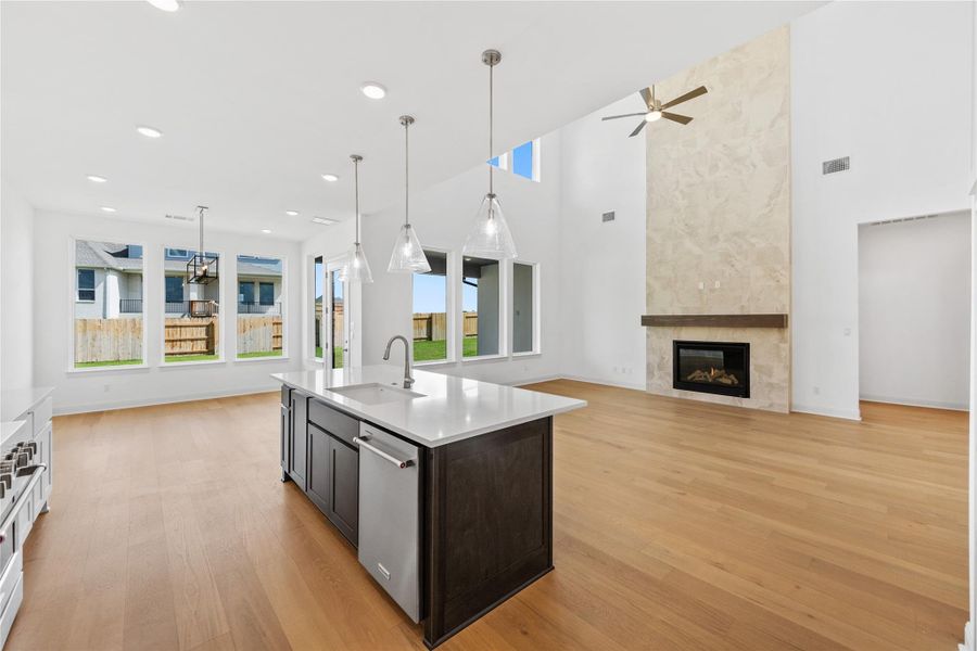 Dual tone kitchen with a high ceiling, open floor plan, a fireplace, decorative light fixtures, and an island with sink