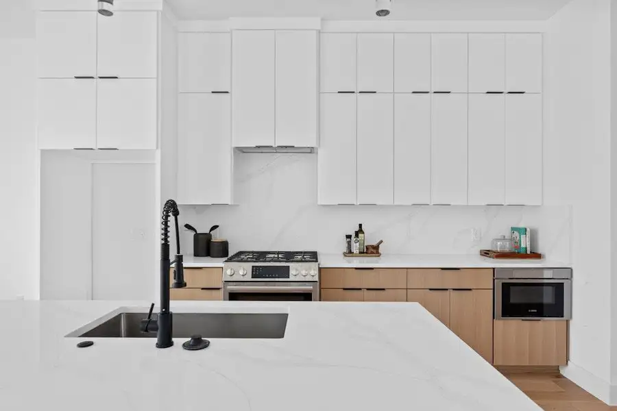 Kitchen featuring modern cabinets, white cabinets, stainless steel appliances, and light stone counters