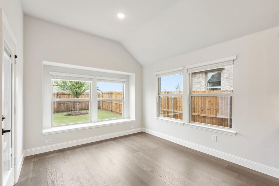 Empty room with vaulted ceiling, hardwood floors, and large windows overlooking fenced backyard Empty room with vaulted ceiling, hardwood floors, and large windows overlooking fenced backyard