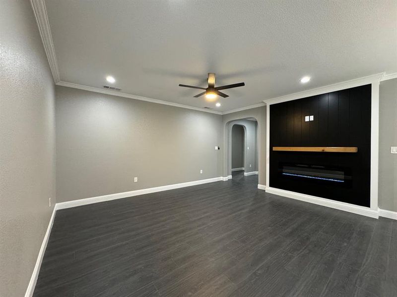 Unfurnished living room with dark hardwood / wood-style floors, ceiling fan, and ornamental molding