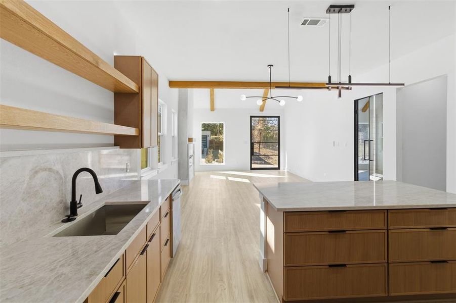 Kitchen with open shelves, wood finish cabinetry, light wood-style flooring, light stone counters, and open floor plan