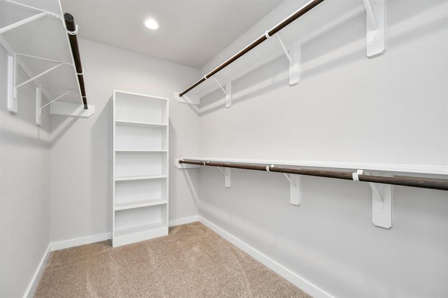 Experience luxury in this spacious walk-in closet with high ceilings and plush carpet. Warm paint tones, built-in shelving, and dark finishes create a contemporary and functional retreat. Sample photo of completed home with similar floor plan. As-built interior colors and selections may vary.