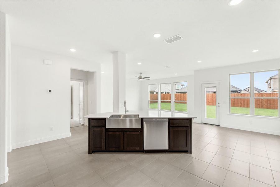 Kitchen island with dark cabinets, farmhouse sink, and stainless dishwasher on tile floors with backyard windows Kitchen island with dark cabinets, farmhouse sink, and stainless dishwasher on tile floors with backyard windows