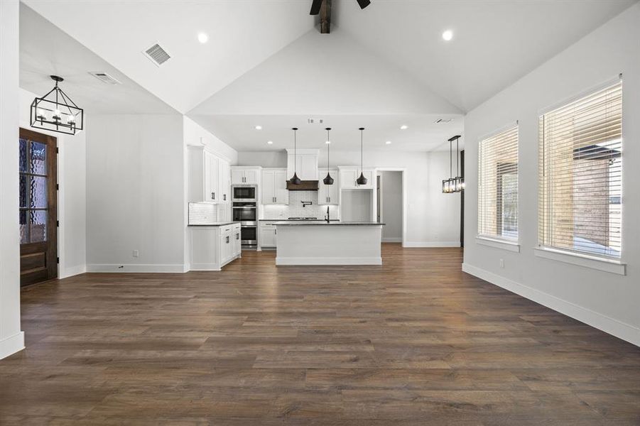 Unfurnished living room featuring a chandelier, healthy amount of natural light, and dark wood-style floors