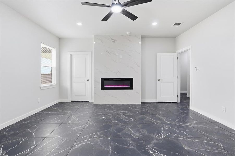 Spacious room featuring sleek dark tile flooring with white veining, a floor-to-ceiling white marble-look fireplace surround with an electric fireplace insert, and a contemporary ceiling fan with integrated lighting