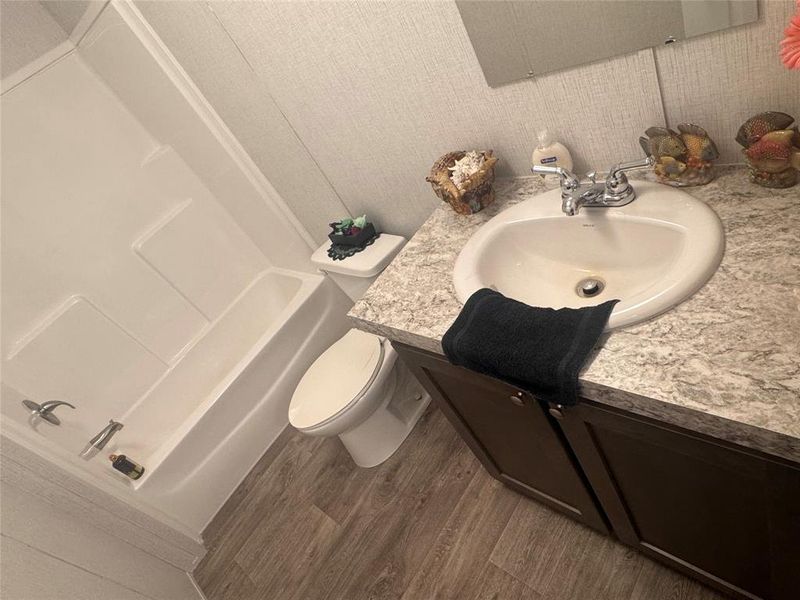 Bathroom featuring vanity, dark wood-type flooring, shower / bathtub combination, and wallpapered walls Bathroom featuring vanity, dark wood-type flooring, shower / bathtub combination, and wallpapered walls
