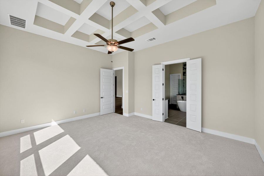 Unfurnished bedroom with coffered ceiling, light carpet, ceiling fan, beam ceiling, and connected bathroom Unfurnished bedroom with coffered ceiling, light carpet, ceiling fan, beam ceiling, and connected bathroom