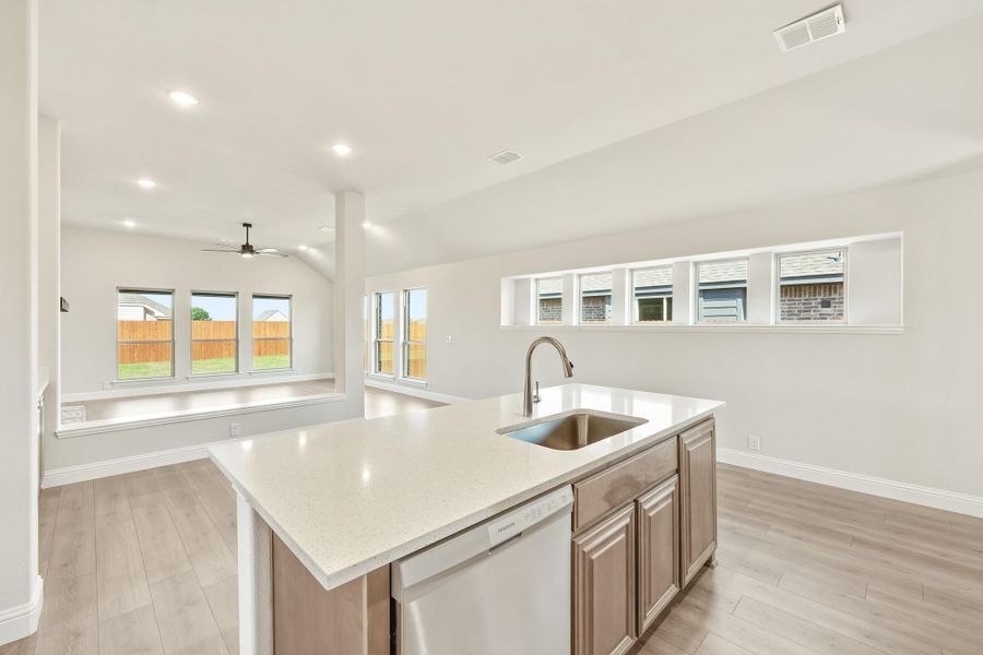 Kitchen island with quartz countertop, stainless sink, and dishwasher, open to living area with light wood floors Kitchen island with quartz countertop, stainless sink, and dishwasher, open to living area with light wood floors