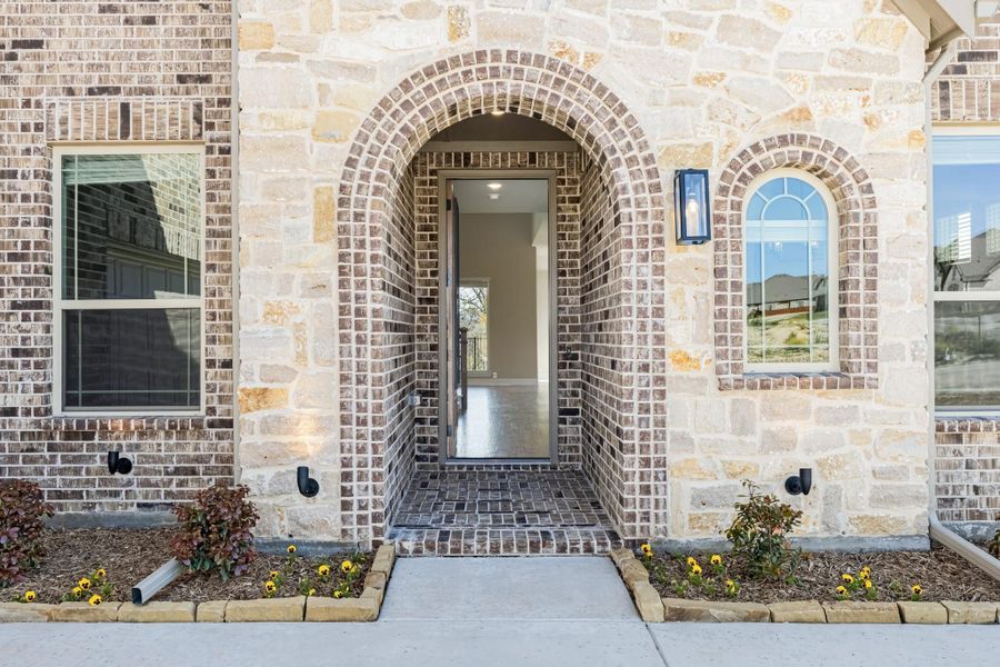 Home entrance with brick arched doorway, stone exterior, and small flower beds along the walkway