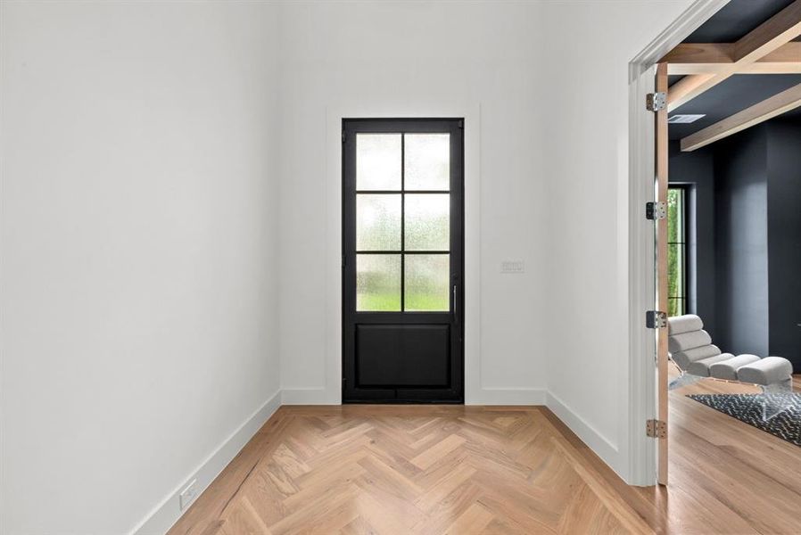 Entryway featuring hardwood floors with a herringbone pattern, a black grid-paneled door with frosted glass, and white walls