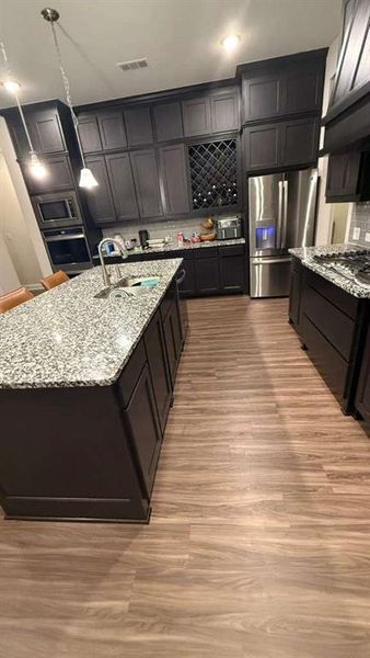Kitchen featuring light stone countertops, light wood-style floors, hanging light fixtures, stainless steel appliances, and backsplash