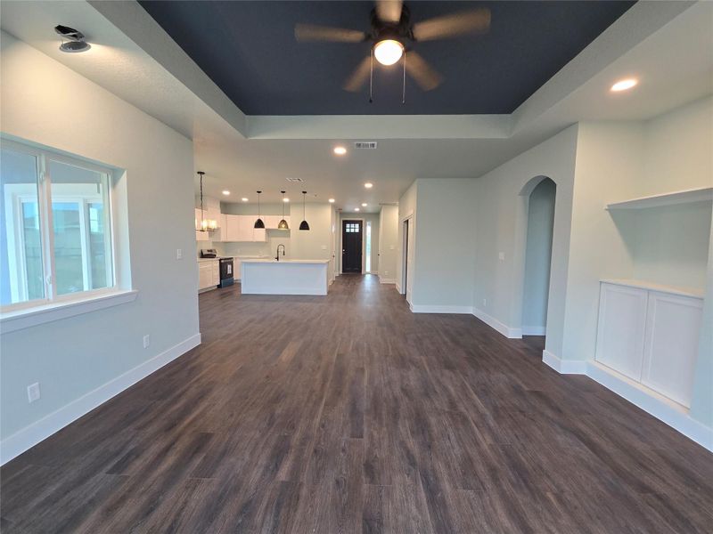 Unfurnished living room featuring recessed lighting, dark wood-style flooring, a ceiling fan, and a tray ceiling