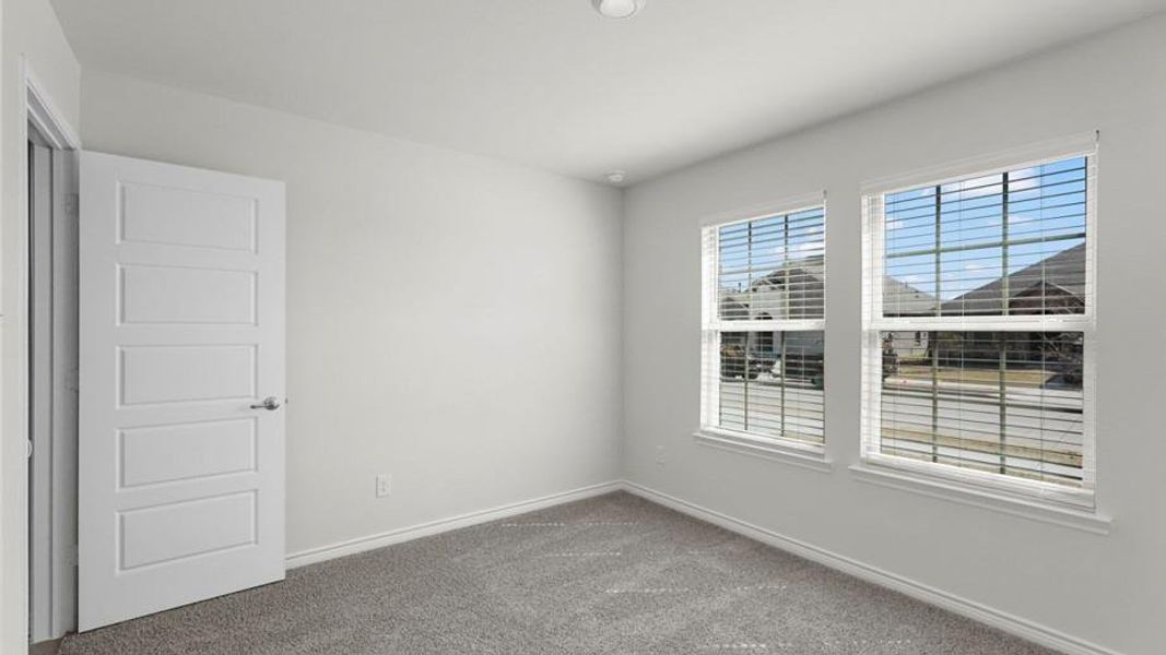 Neutral-toned room featuring a five-panel interior door with brushed nickel hardware, light gray carpeting, and two double-hung windows with blinds