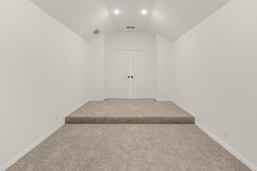 Empty room with vaulted ceiling, beige carpet, raised platform, and white double doors