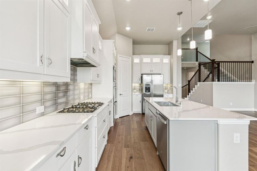 Kitchen featuring dark wood-style floors, appliances with stainless steel finishes, tasteful backsplash, white cabinets, and hanging light fixtures