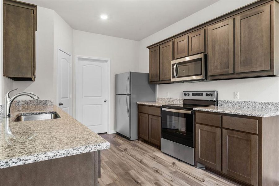 Kitchen with dark brown cabinetry, stainless steel appliances, light wood-type flooring, a sink, and recessed lighting