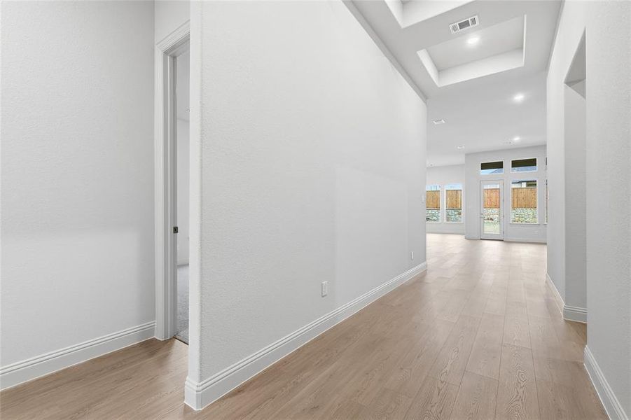 Hall with light wood finished floors, recessed lighting, and a tray ceiling