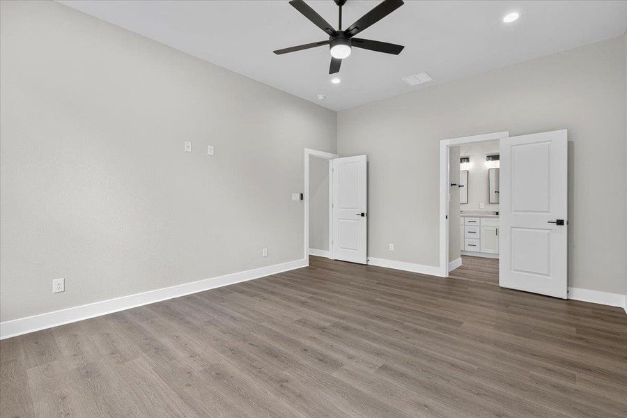 A spacious primary bedroom features durable wood-look flooring and a modern ceiling fan, offering direct access to an en-suite bathroom. A spacious primary bedroom features durable wood-look flooring and a modern ceiling fan, offering direct access to an en-suite bathroom.