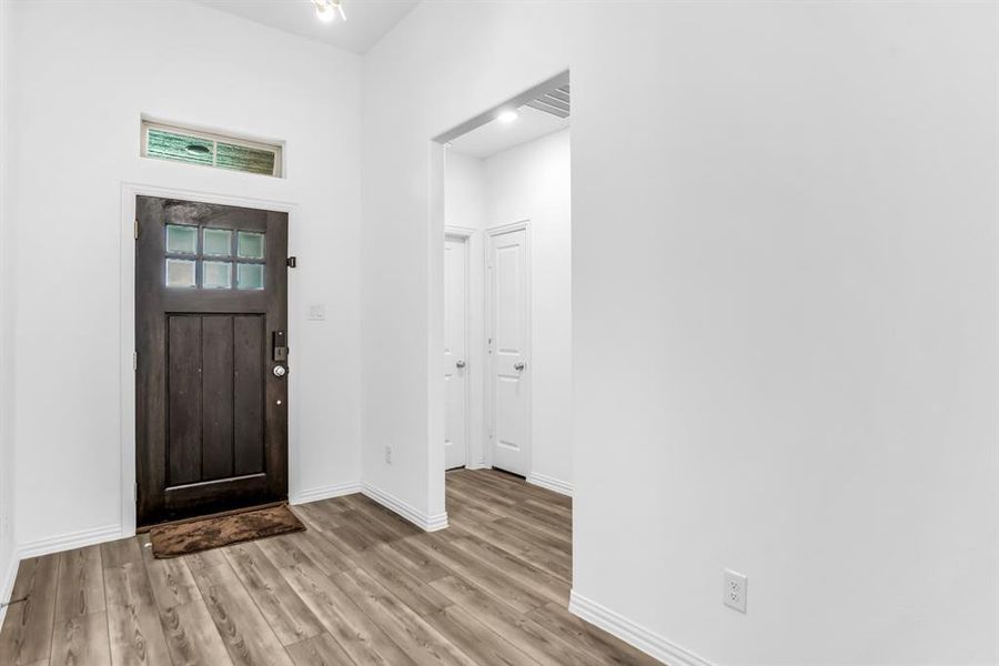Entryway featuring a dark wood-finish door with frosted glass panes, a transom window, wood-finish flooring, and crisp white walls