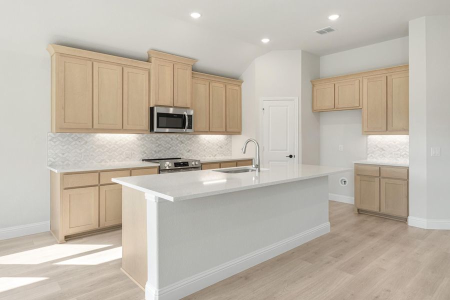 Kitchen with light wood cabinets, center island with sink, stainless steel appliances, and light wood floors