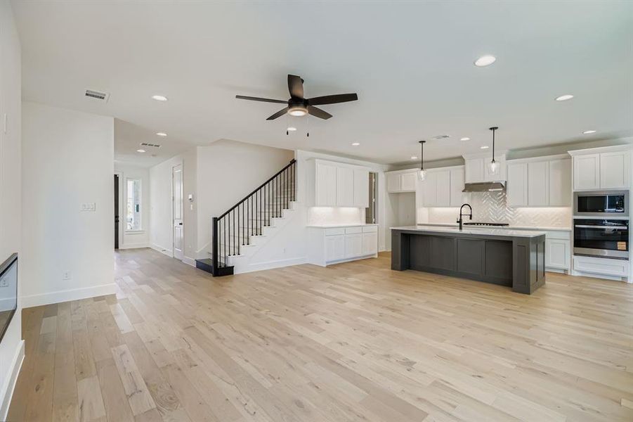 Kitchen featuring open floor plan, white cabinetry, decorative light fixtures, backsplash, and light wood finished floors