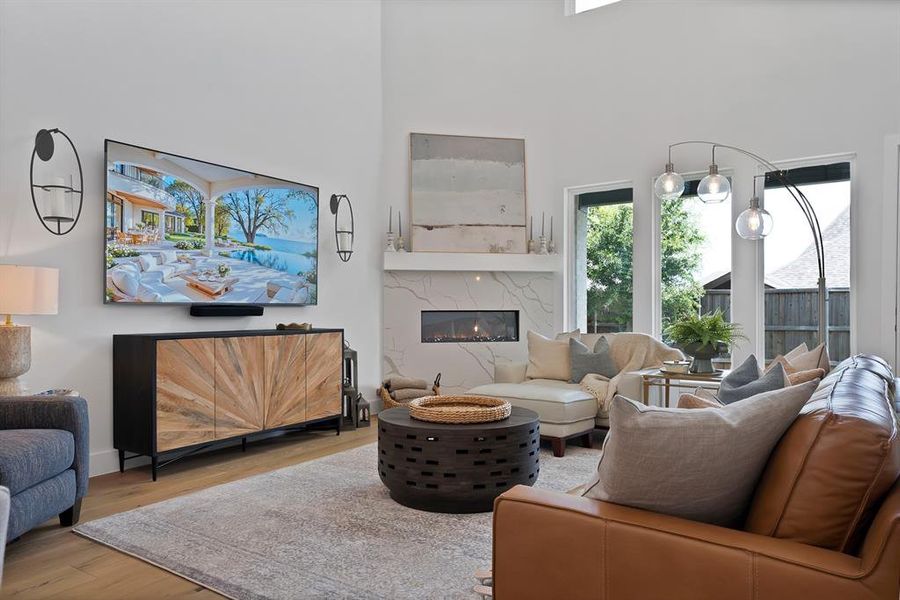 Spacious living area featuring a vaulted ceiling, a linear gas fireplace with a stone surround, and wood-finish flooring Spacious living area featuring a vaulted ceiling, a linear gas fireplace with a stone surround, and wood-finish flooring