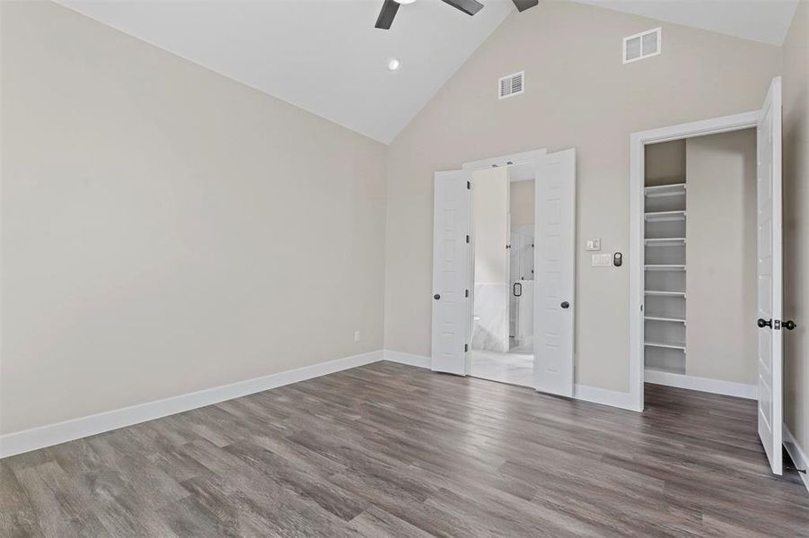 Unfurnished bedroom with a closet, a spacious closet, ceiling fan, dark wood-type flooring, and high vaulted ceiling