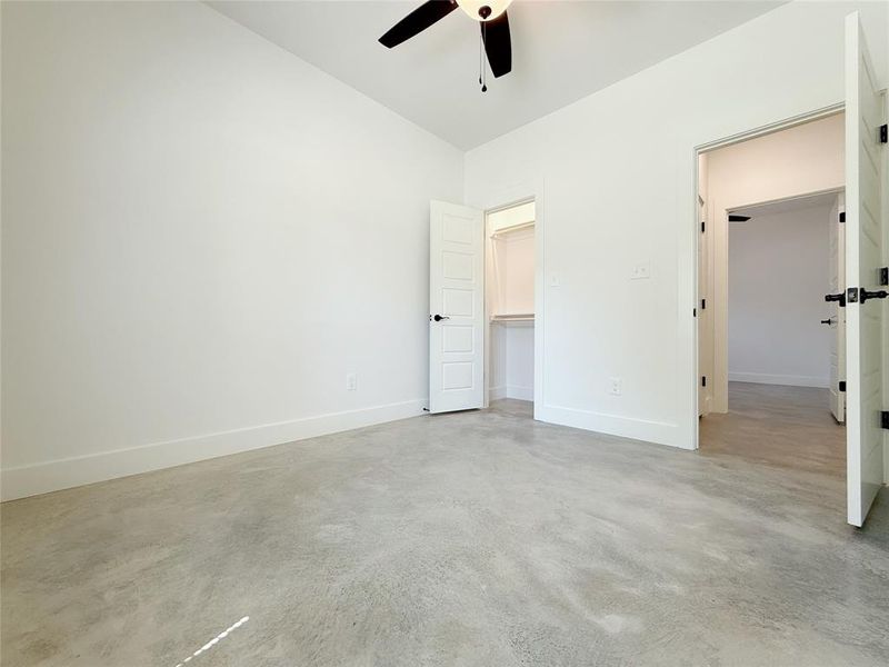 Unfurnished bedroom featuring finished concrete flooring, baseboards, a spacious closet, and a ceiling fan Unfurnished bedroom featuring finished concrete flooring, baseboards, a spacious closet, and a ceiling fan
