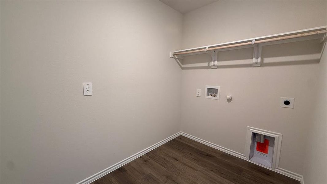 Dedicated utility space featuring wood-finish flooring, light gray walls, white baseboards, and a built-in wall shelf with a clothing rod