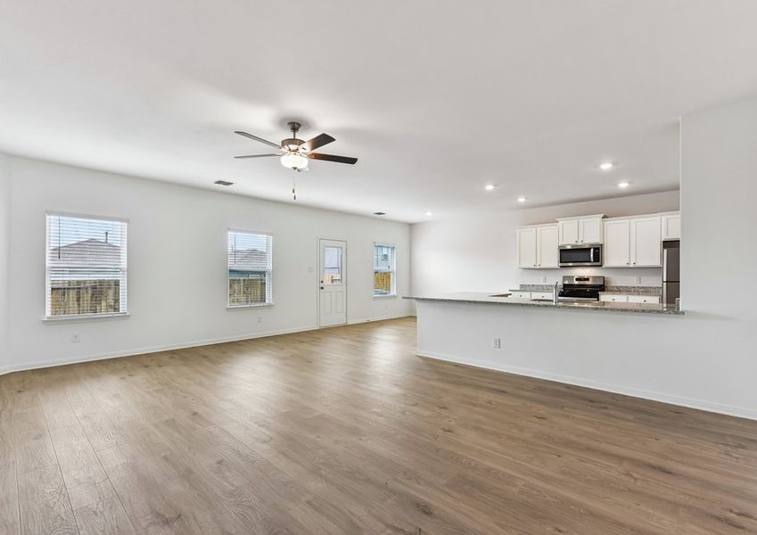 Open-concept family room featuring a ceiling fan, wood-look vinyl flooring, and a sightline into the kitchen.