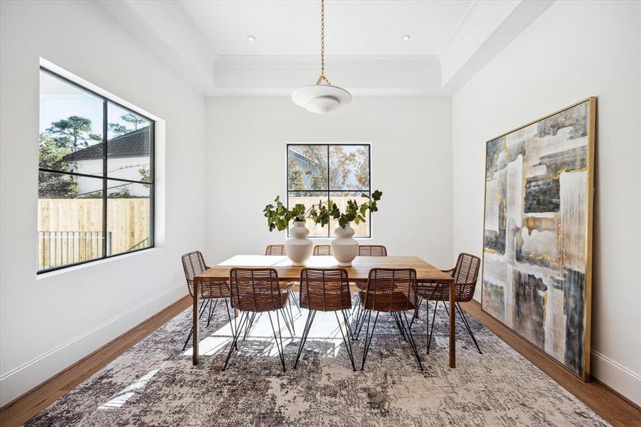 This charming breakfast room features two steel windows that overlook the wraparound covered patio, offering beautiful treetop views. Illuminated by a designer plaster chandelier and grounded by European white oak floors, the space is perfect for enjoying morning coffee in a serene setting.