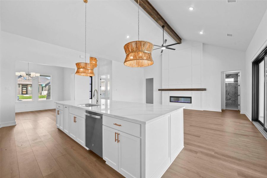 Kitchen featuring high vaulted ceiling, pendant lighting, white cabinets, a large island, and light wood finished floors Kitchen featuring high vaulted ceiling, pendant lighting, white cabinets, a large island, and light wood finished floors