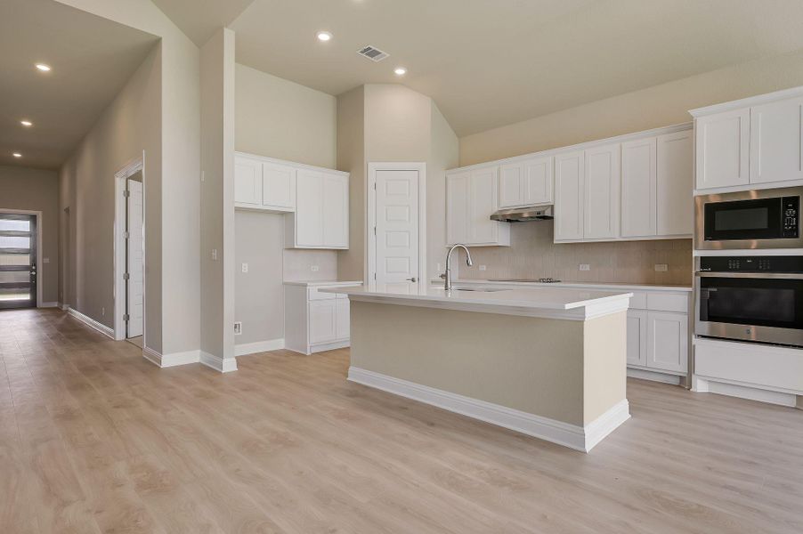 Kitchen with stainless steel oven, white cabinetry, light wood-type flooring, an island with sink, and recessed lighting
