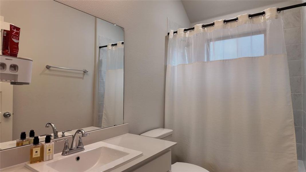 Well-appointed bathroom featuring a vanity with an integrated sink and a large mirror, alongside a shower with a privacy window