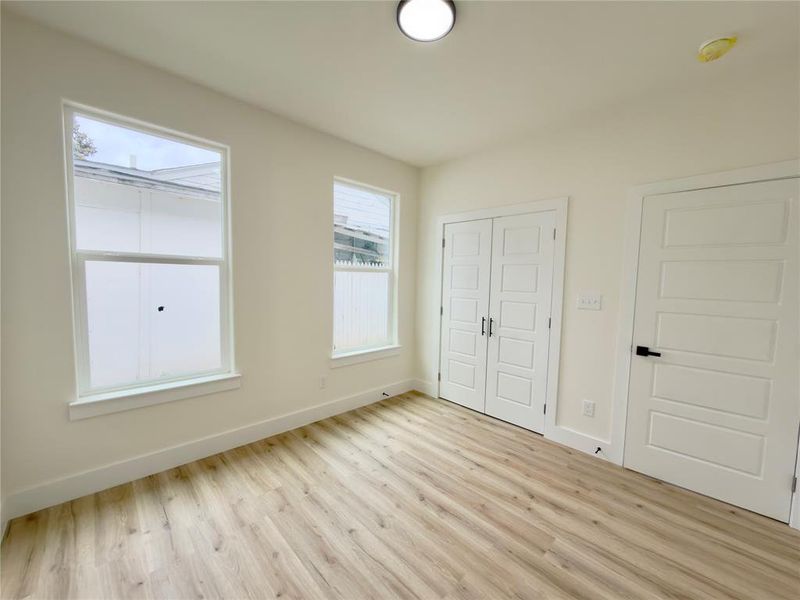 Bright room featuring wood-finish flooring, two large windows, a pair of panel-style bifold doors, and a single panel-style door with matte black hardware