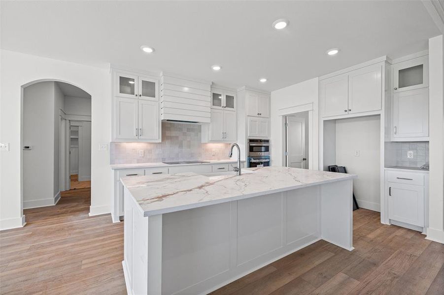 Kitchen featuring a large central island with a stone-finish countertop, white cabinetry, wood-finish flooring, a tile backsplash, and recessed lighting