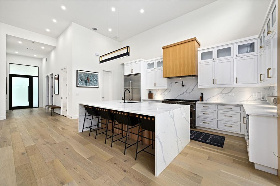 Kitchen with high end appliances, light wood finished floors, a spacious island, a sink, and a towering ceiling