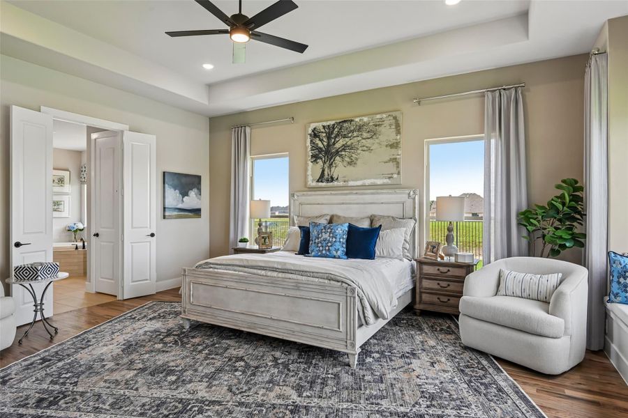 Master bedroom with tray ceiling, ceiling fan, hardwood floors, and two windows with natural light Master bedroom with tray ceiling, ceiling fan, hardwood floors, and two windows with natural light