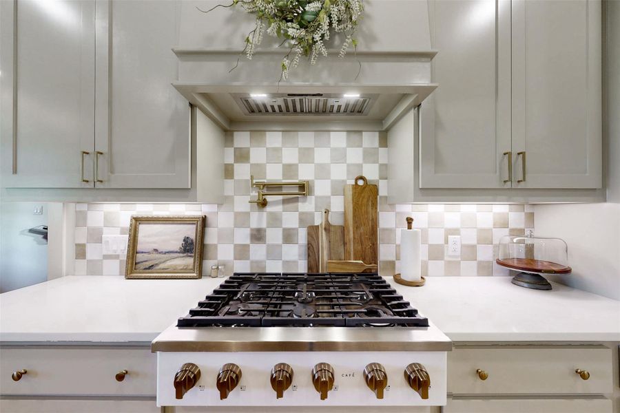 Kitchen featuring light countertops, exhaust hood, backsplash, and stainless steel gas stovetop backsplash, ventilation hood, light countertops, and stainless steel gas stovetop