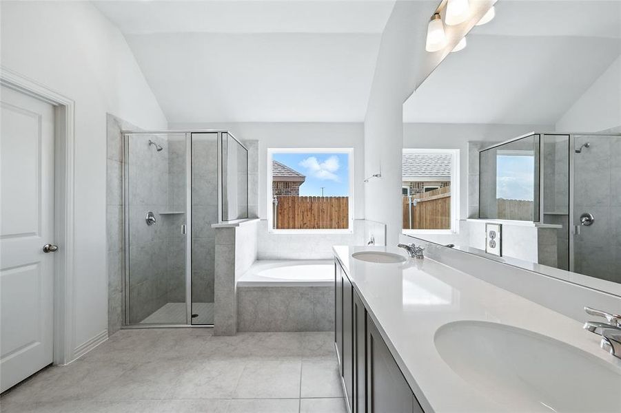 Full bathroom featuring a bath, a shower stall, lofted ceiling, double vanity, and light tile patterned floors Full bathroom featuring a bath, a shower stall, lofted ceiling, double vanity, and light tile patterned floors