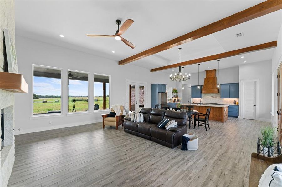 Spacious living area featuring wood-finish flooring, exposed ceiling beams, and a stone-clad fireplace