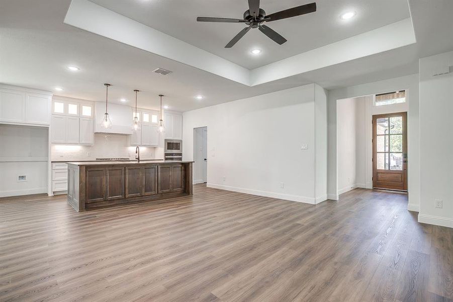 Unfurnished living room with a tray ceiling, recessed lighting, a ceiling fan, and dark wood-type flooring