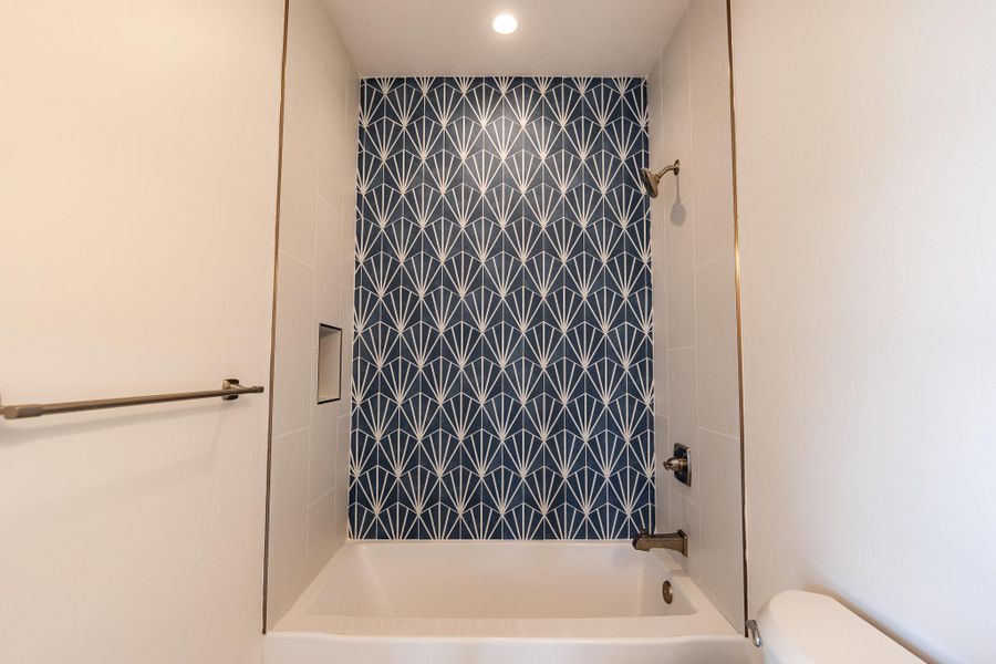A striking patterned tile accent wall provides a bold backdrop to this pristine bathroom tub and shower. A striking patterned tile accent wall provides a bold backdrop to this pristine bathroom tub and shower.