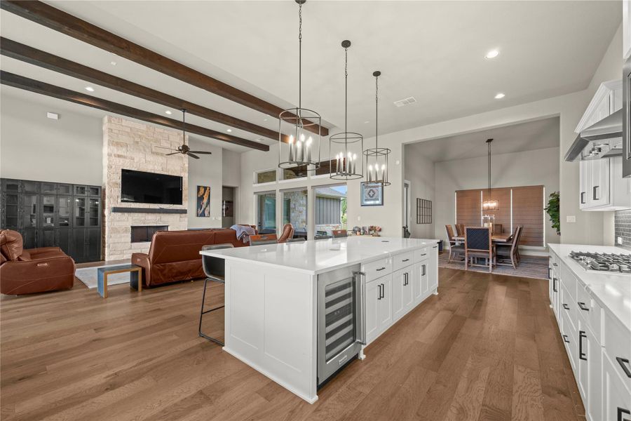 An open-concept living space features exposed beam ceilings, a stone fireplace, and a spacious kitchen island with seating. An open-concept living space features exposed beam ceilings, a stone fireplace, and a spacious kitchen island with seating.