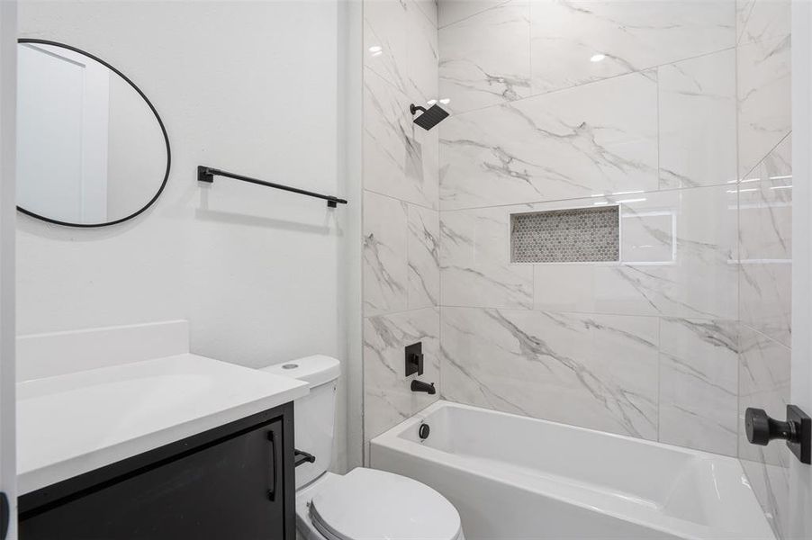Bathroom featuring large format wall tiles, a built-in shower niche with mosaic tile, a dark wood-finish vanity with a white countertop, and matte black fixtures