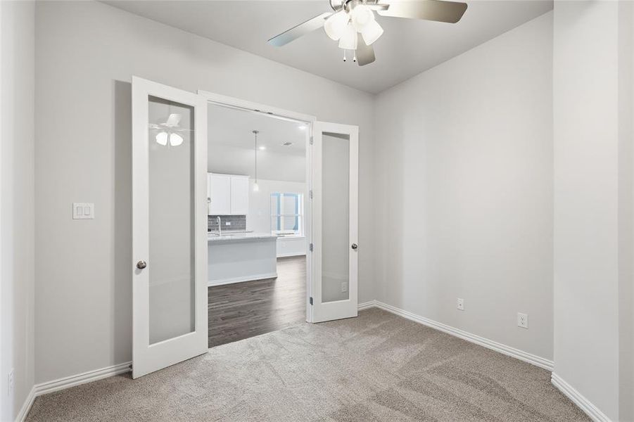 Versatile interior space featuring French doors with frosted glass panels, a ceiling fan with integrated lighting, and neutral carpeting