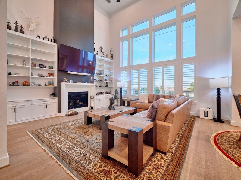 Experience the elegance of a living room with soaring ceilings, expansive windows, a sleek gas fireplace, custom cabinetry, and designer shutters, all offering breathtaking views.