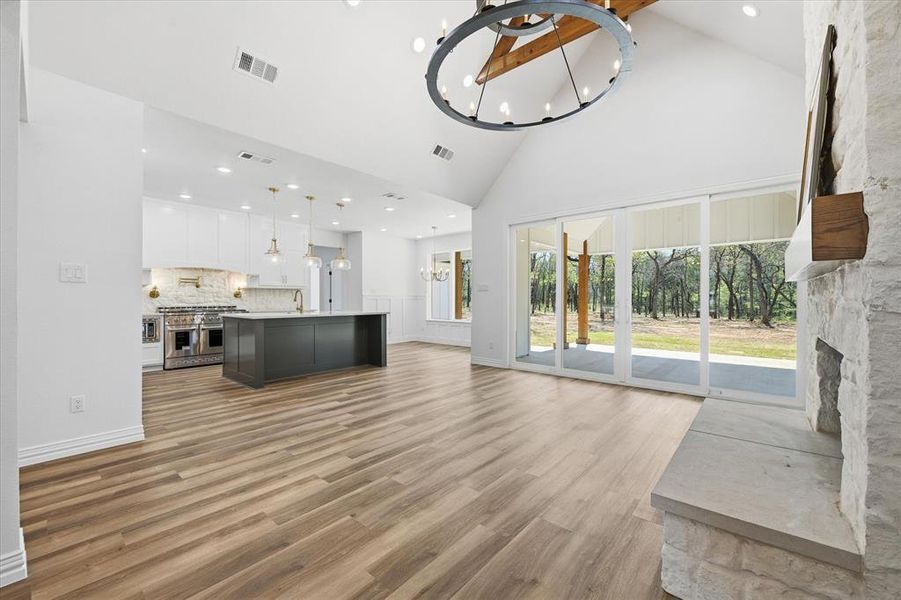 Unfurnished living room with suspended lighting, light wood-style floors, a fireplace, and vaulted ceiling